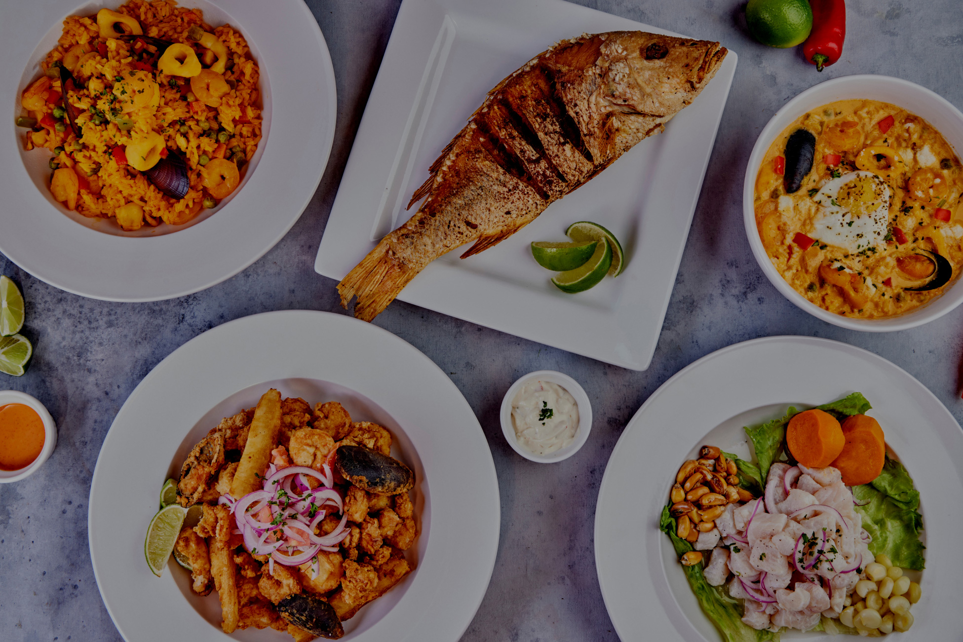 Plates of food on a table. Fried fish, seafood, vegetables, rice, limes, and sauces.