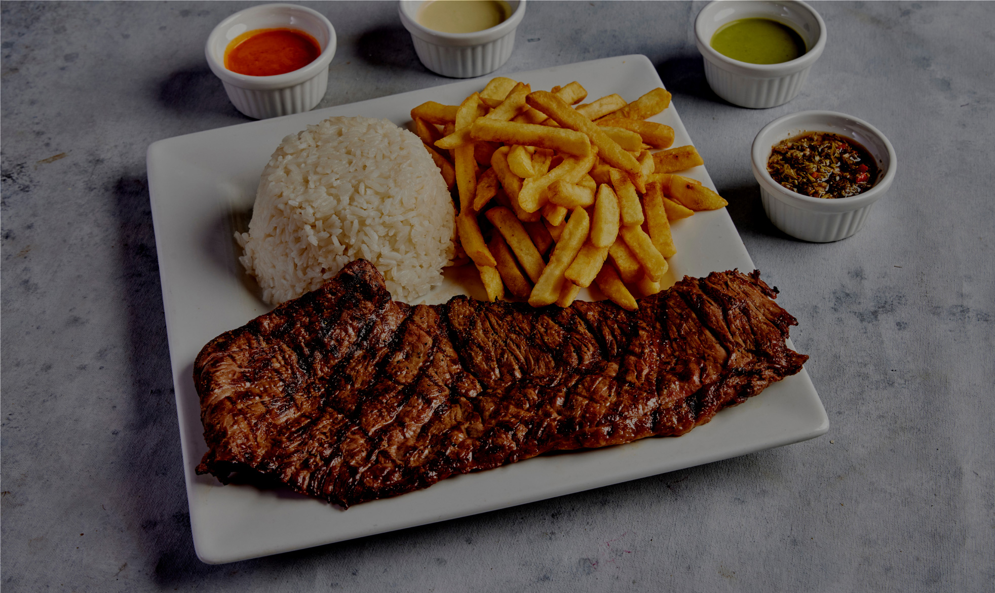 Plate of grilled steak, rice, fries, and sauces